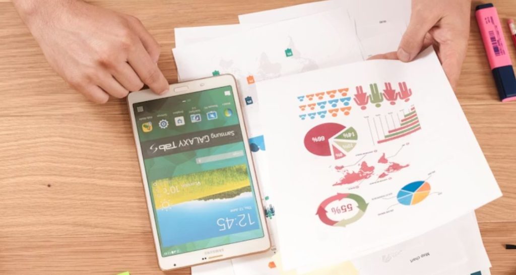 Esta imagem apresenta uma perspectiva superior (vista aérea) de uma estação de trabalho organizada em uma mesa de madeira clara, onde se realiza uma análise de dados híbrida