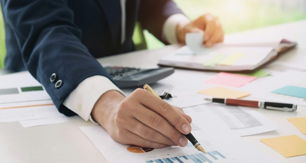 Esta foto retrata um profissional, vestindo um traje formal de negócios com blazer azul e camisa branca, concentrado em uma atividade de análise financeira e planejamento.