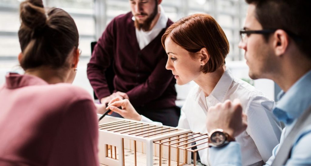 Uma reunião de negócios ou design em close-up, centrada em uma maquete arquitetônica.