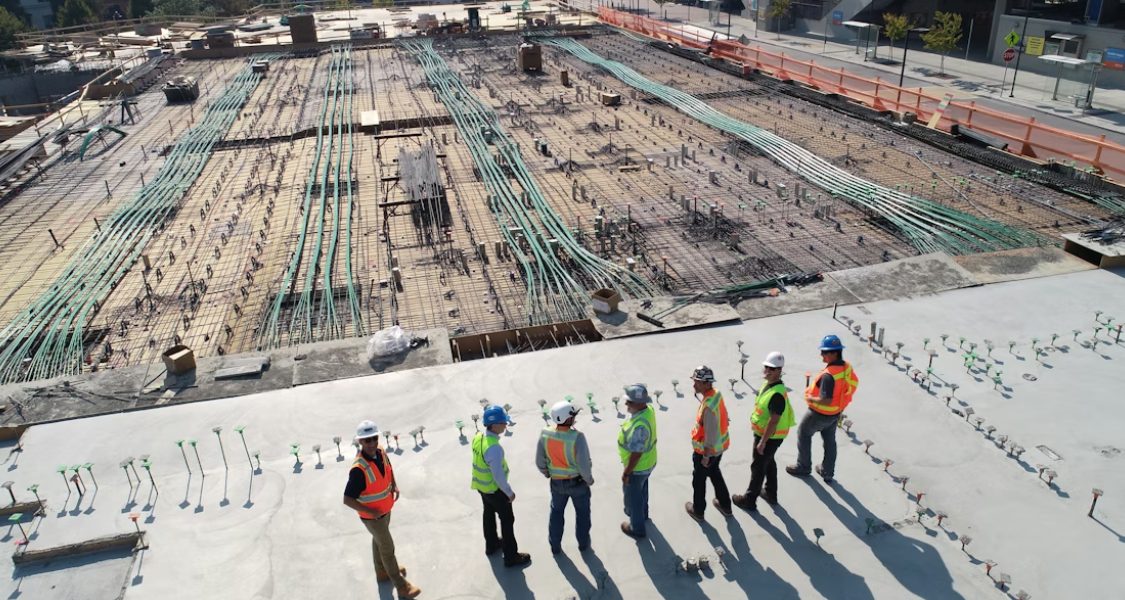 Trata-se de uma fotografia aérea ou de drone que mostra um grande canteiro de obras, focando na fase de fundação ou laje de concreto.