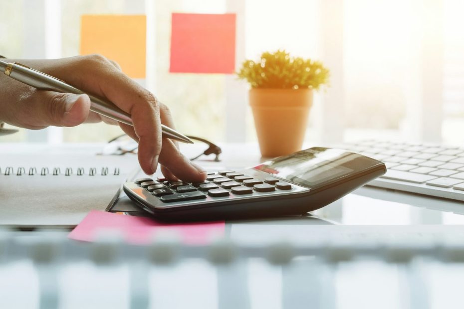 etrata um close-up de uma mão realizando cálculos em uma calculadora, em um ambiente de escritório bem iluminado.