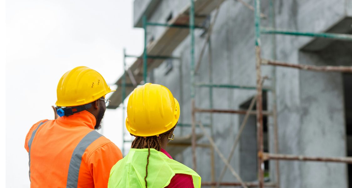 Esta foto retrata dois profissionais de construção ou engenharia, vistos por trás, estão inspecionando uma estrutura em construção.
