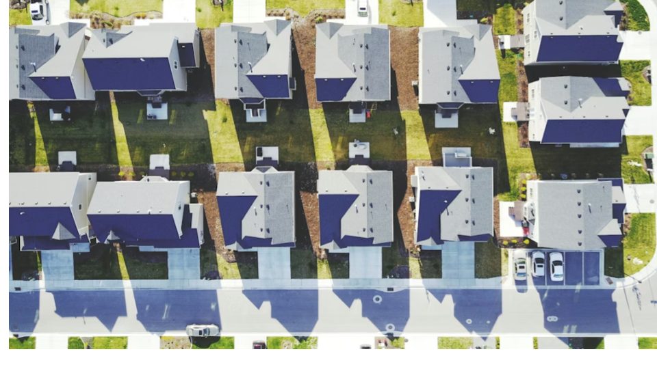 A imagem apresenta uma vista aérea vertical (top-down) de um bairro residencial planejado, com casas organizadas de forma simétrica ao longo de uma rua.