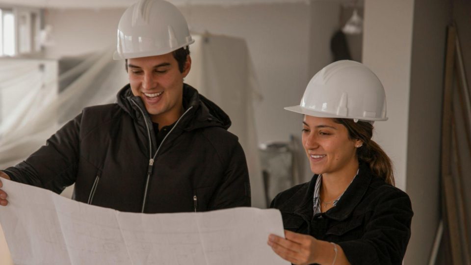 Esta imagem apresenta dois profissionais em um canteiro de obras, focando na colaboração e no planejamento técnico durante a execução de um projeto.