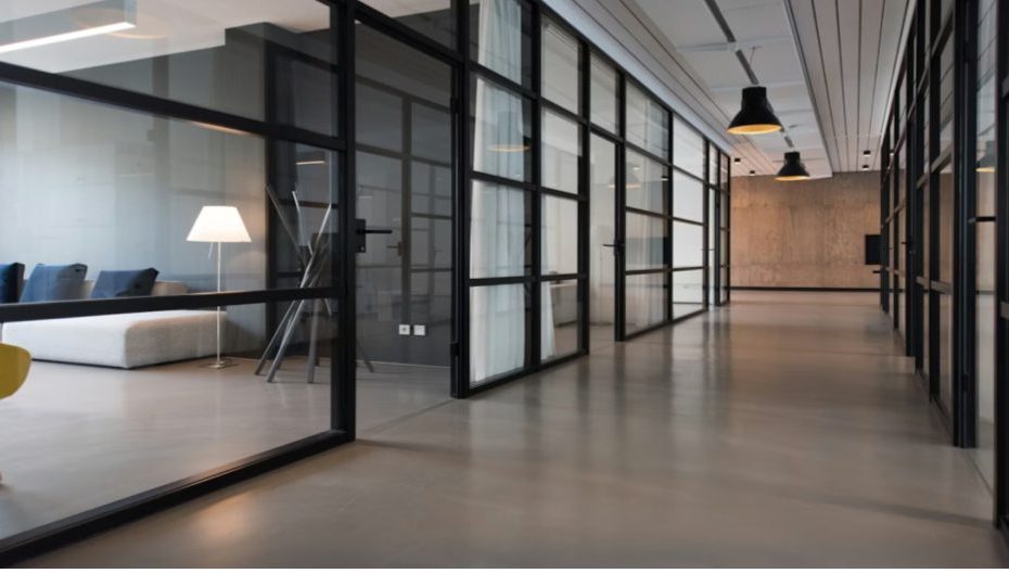 Esta imagem apresenta um corredor de um escritório moderno, caracterizado por um design minimalista, industrial e sofisticado.