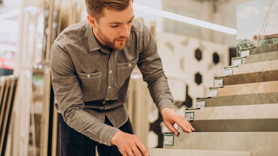 Esta imagem retrata um homem escolhendo revestimentos em uma loja de materiais de construção ou showroom de design.