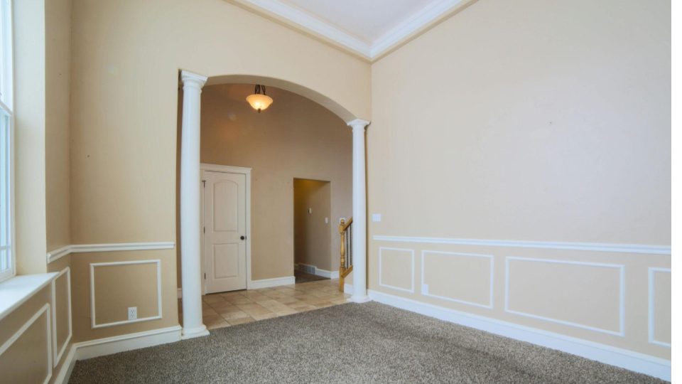 A imagem mostra um ambiente interno vazio, com acabamento residencial clássico e cores neutras. As paredes são pintadas em tom bege claro, com molduras brancas em meia altura (boiserie simples) que acrescentam elegância ao espaço.