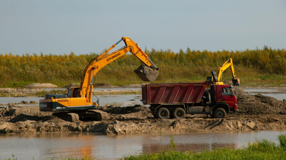 Uma cena de canteiro de obras ou área de extração próxima a um corpo d'água.