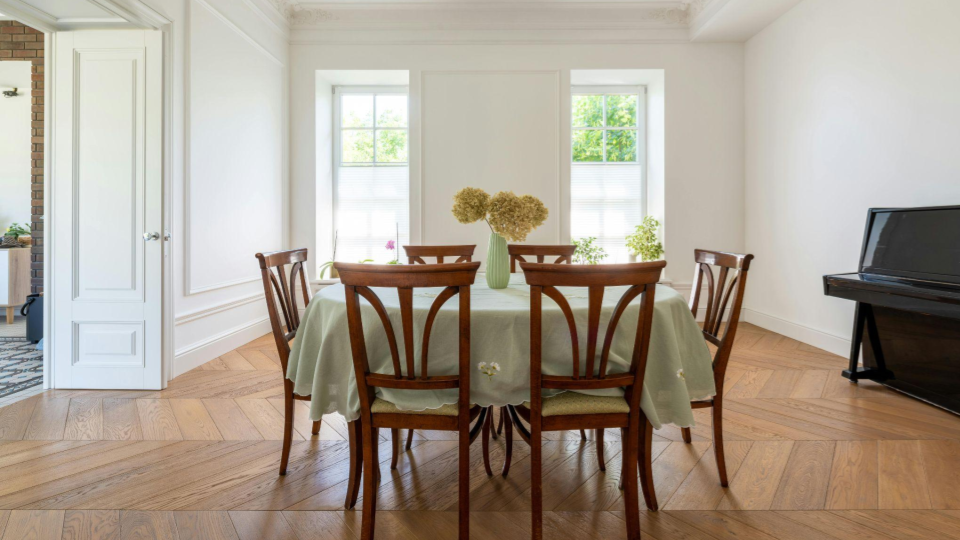 Um sofá de estampa clássica posicionado à frente de uma TV montada na parede. Há grandes janelas que garantem muita iluminação natural.