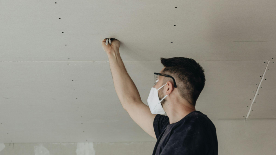 Esta imagem mostra um profissional realizando a instalação elétrica em um forro de drywall. A cena foca no trabalho de acabamento e infraestrutura técnica.