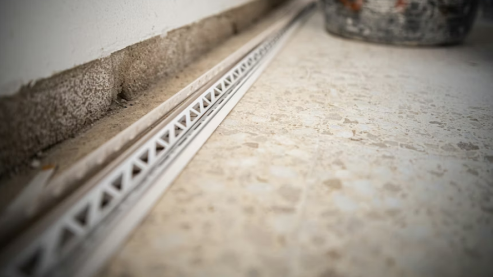 Uma imagem em perspectiva focada no nível do chão, mostrando a transição entre uma parede de blocos e um piso de granilite ou concreto polido.
