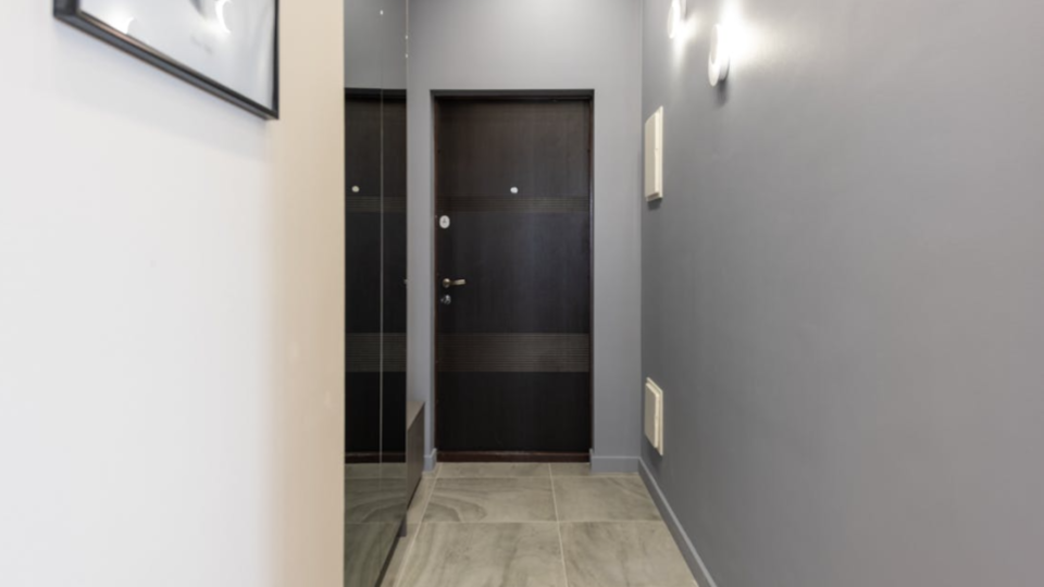 A imagem mostra o corredor ou hall de entrada de um apartamento moderno com uma paleta de cores sóbria e contemporânea.