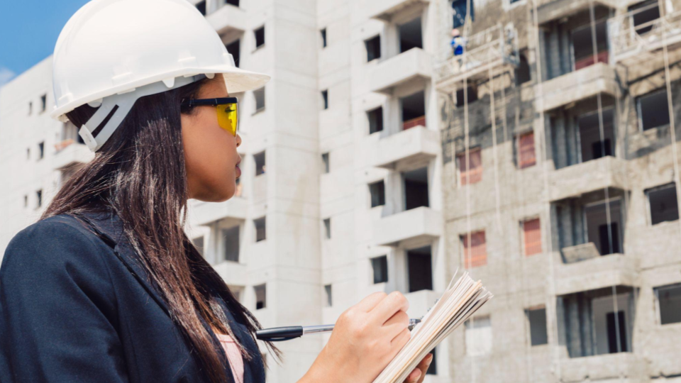 A imagem mostra o perfil de uma mulher trabalhando em um canteiro de obras de grande porte.