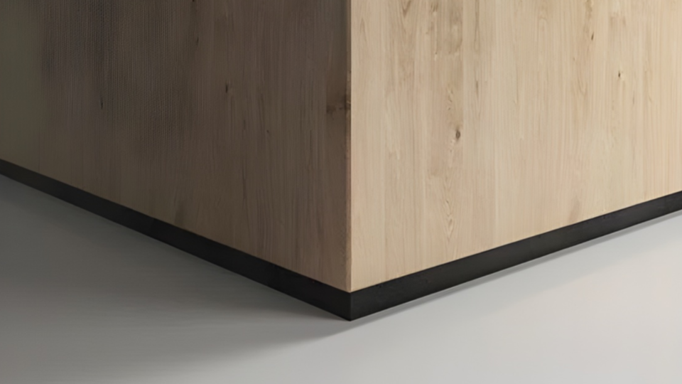 Detalhe de um rodapé preto instalado na base de um painel de madeira clara, com acabamento minimalista e moderno.
