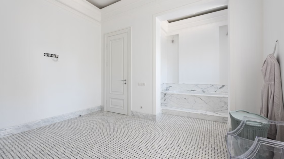 Esta imagem mostra o interior de um ambiente amplo e luxuoso em fase de finalização, combinando elementos da arquitetura clássica com acabamentos modernos, possivelmente uma suíte master com integração para a área de banho.
