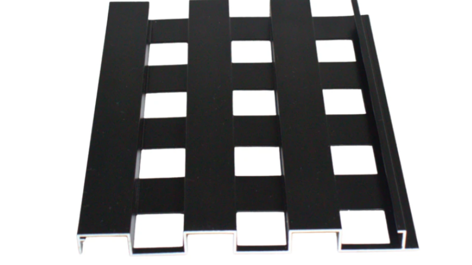 Detalhe aproximado de um painel ou perfil metálico preto vazado com padrão quadriculado regular, exibindo recortes geométricos precisos.