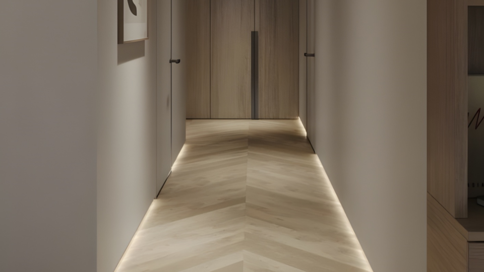 Corredor moderno de design limpo com piso de madeira em escama de peixe (chevron) e fita de LED embutida rente ao chão, criando uma iluminação indireta e acolhedora.