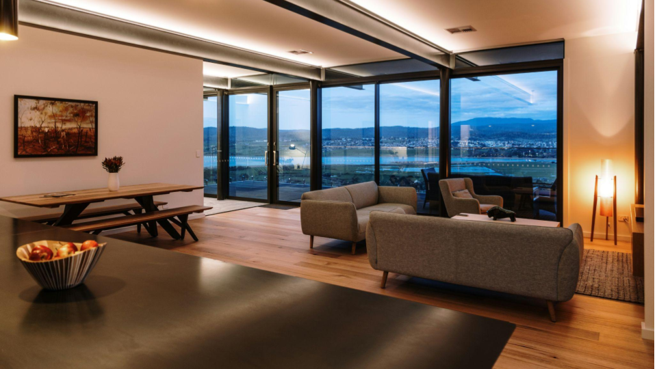 A imagem retrata o interior de uma residência moderna e integrada em conceito aberto durante o crepúsculo.