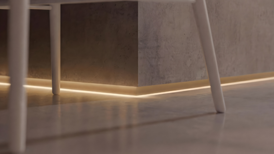 Close-up do canto inferior de uma parede cinza com acabamento de cimento queimado. Destaca-se um rodapé com fita de LED embutida que projeta uma luz quente e suave diretamente no piso polido, entre os pés de uma cadeira branca.
