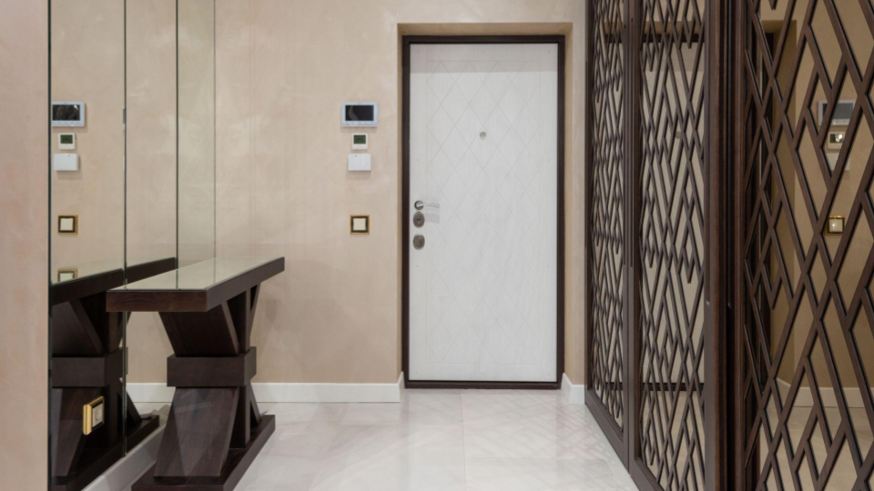 Ambiente de recepção/hall residencial com parede espelhada, console de madeira escura com tampo de vidro, porta de entrada branca e um painel de madeira com treliça geométrica cobrindo a parede oposta.
