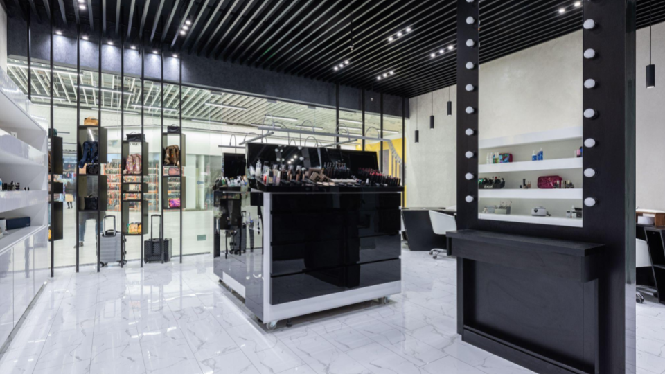 Interior moderno de uma loja de cosméticos e maquiagem com espelho de camarim, balcão preto e piso claro.