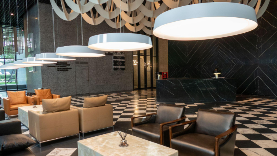 A imagem mostra o lobby moderno e elegante de um hotel ou edifício corporativo, caracterizado por um design contemporâneo de alto padrão.