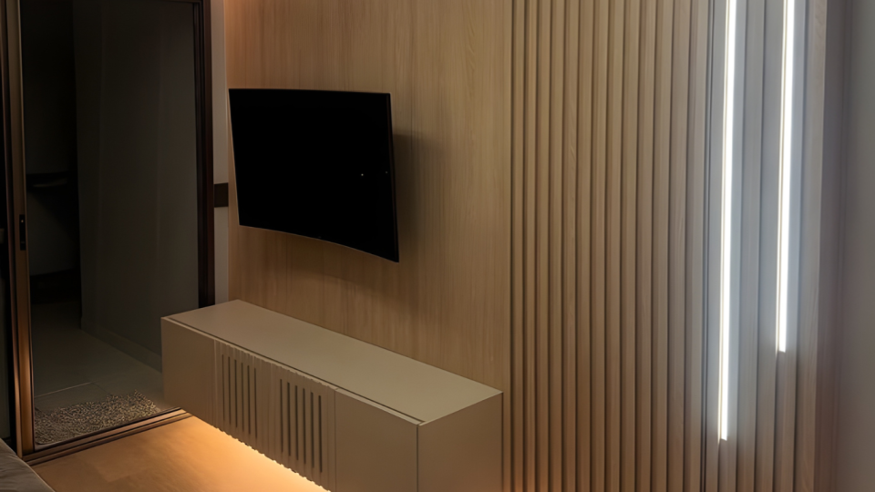 Painel de TV com madeira ripada e iluminação indireta
Móvel planejado com rack suspenso branco, TV fixada na parede, lâmina de madeira clara, ripado vertical e fitas de LED embutidas.